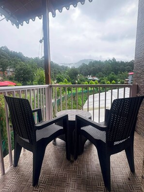Ein Balkon mit zwei Stühlen und einem Tisch, mit Blick auf einen Fluss und viel Grün.