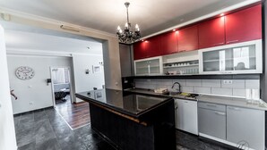 A modern kitchen with a central island, red cabinets, and a chandelier. - Suite Donna (Bihac)