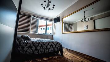 Ein Schlafzimmer mit einem großen Bett, einer Chandelüster, einem Spiegel und einem Fenster mit Jalousien.
