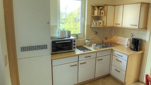 A compact kitchen with a built-in oven, a microwave, and a sink. There is a window providing natural light, and the kitchen has a simple, functional design with light-colored cabinets and a tiled floor. - Fewos am Hafen (Sellin)