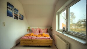 A bedroom with a sloped ceiling, a wooden bed, a radiator, and a window with a view of trees. - Fewos am Hafen (Sellin)