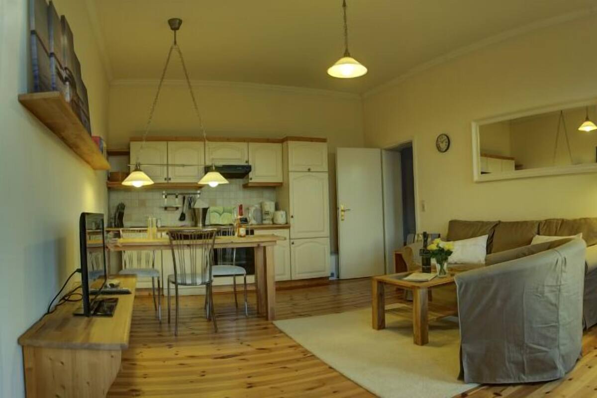 Ein gemütliches Wohnzimmer mit einer Couch, einem Esstisch und einer Küchenzeile mit Schränken und einem Kühlschrank.