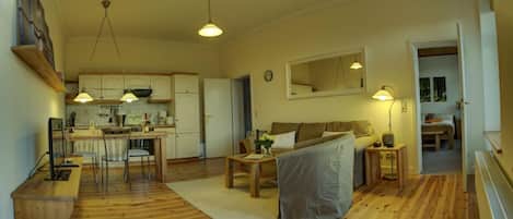 A cozy living room with a sofa, a dining table, and a kitchen area with cabinets and a refrigerator.