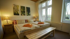 A bedroom with two wooden beds, a bench, two bedside lamps, and a window with curtains. - Fewos am Hafen (Sellin)