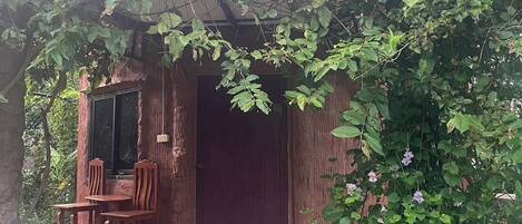 A rustic wooden structure with a door and a small porch area with a table and chairs.