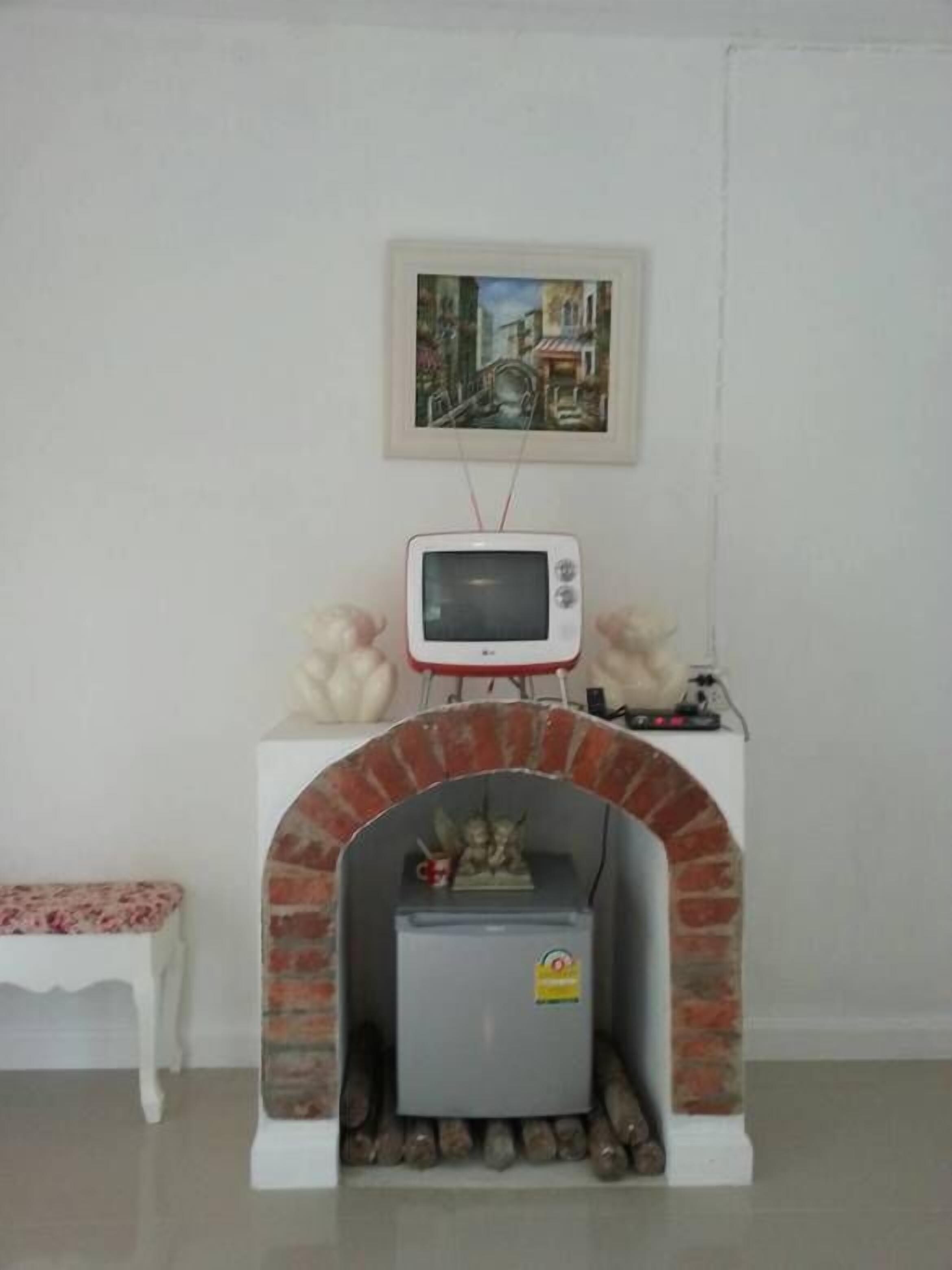 Habitació amb paret blanca, un quadre amb marc, un televisor blanc sobre una estructura de maó i una petita banca.
