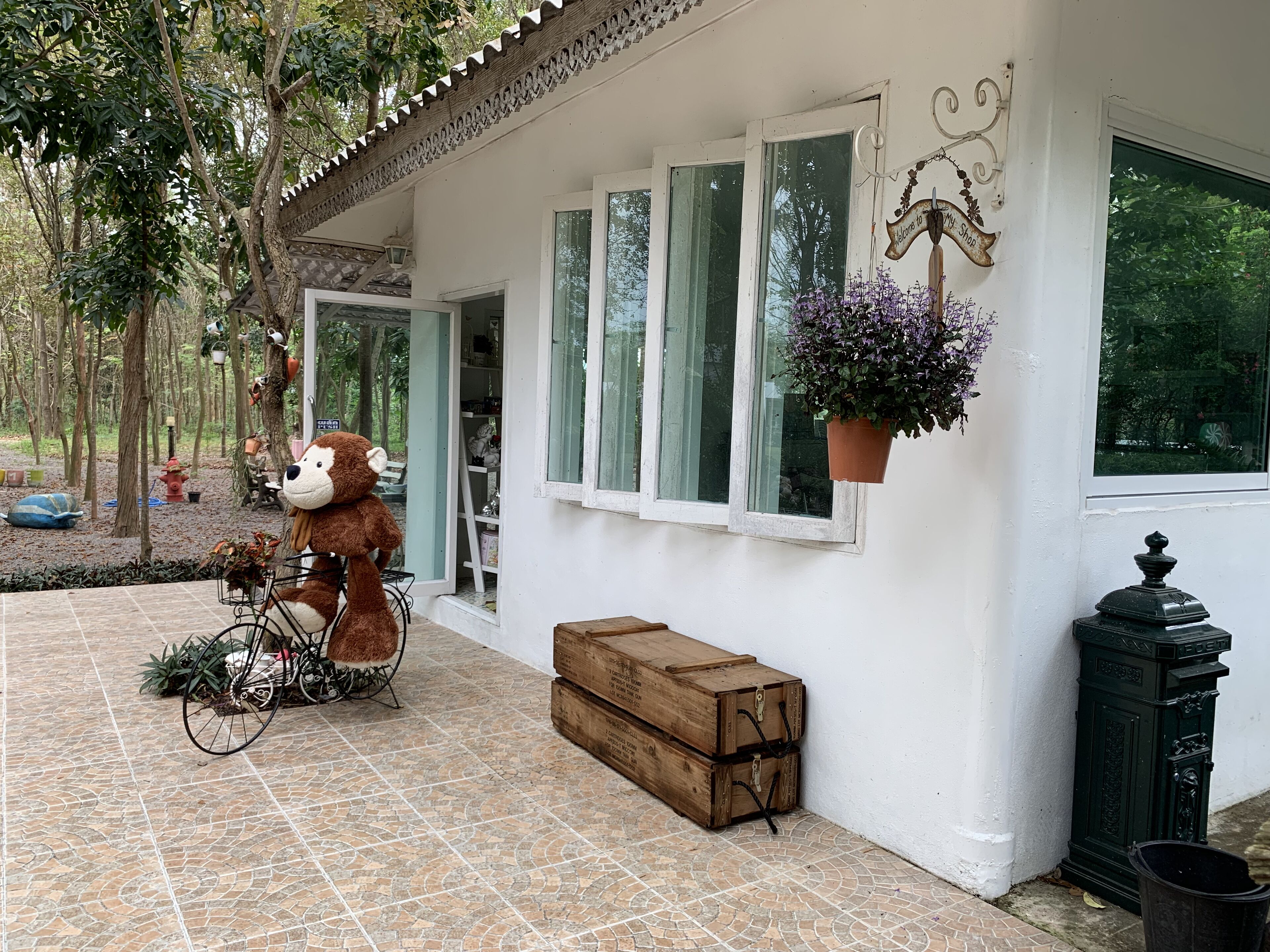 A building with a tiled patio, a wooden bench, a bicycle, a large stuffed animal, and a hanging flower pot.