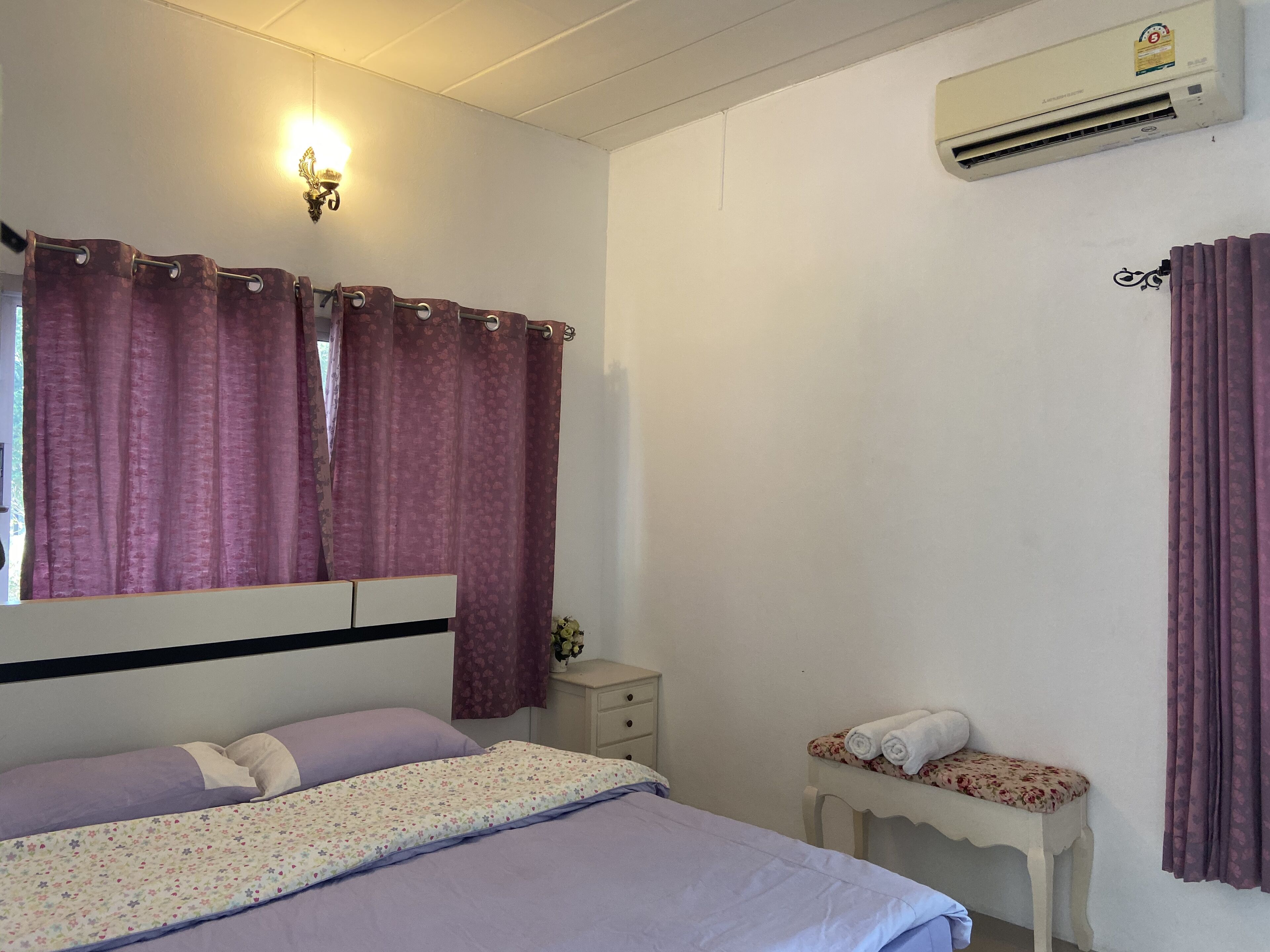 A bedroom with a bed, a nightstand, an air conditioning unit, and a window with curtains.
