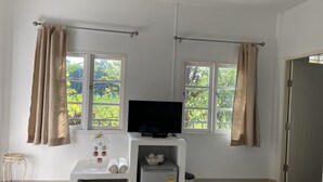 Una habitación pequeña y limpia con televisión, un refrigerador pequeño y una ventana con cortinas.
