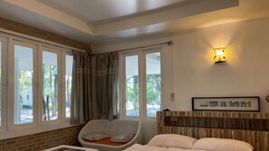 Un dormitorio con una cama, una silla, una mesita y un estante en la pared.