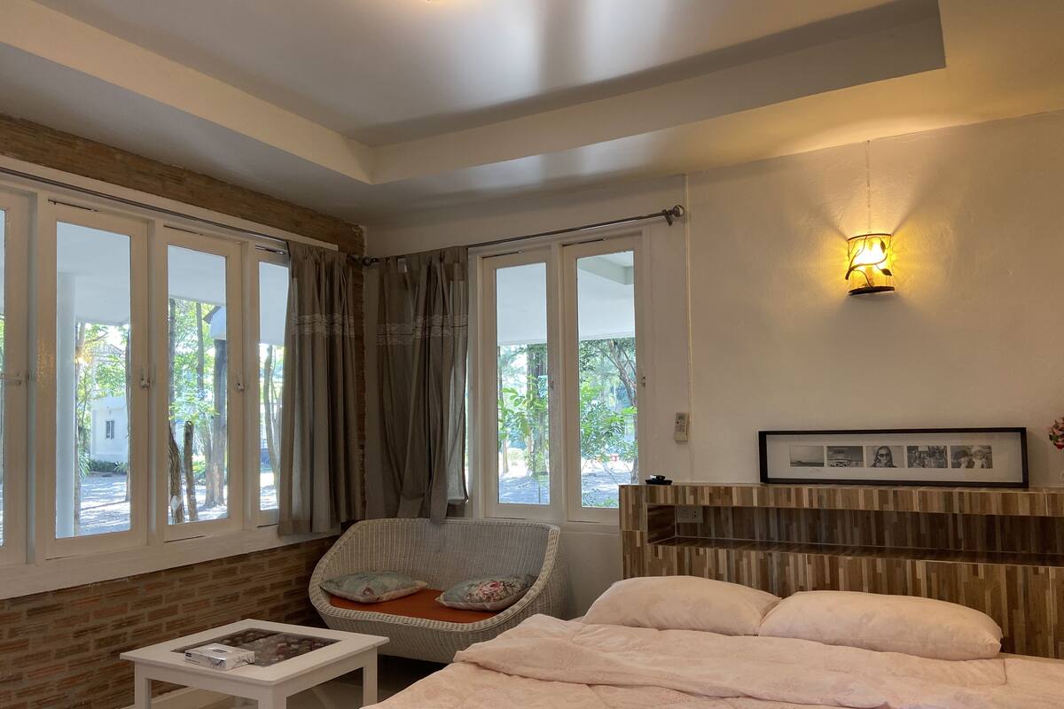 A bedroom with a bed, a chair, a small table, and a wall-mounted shelf.