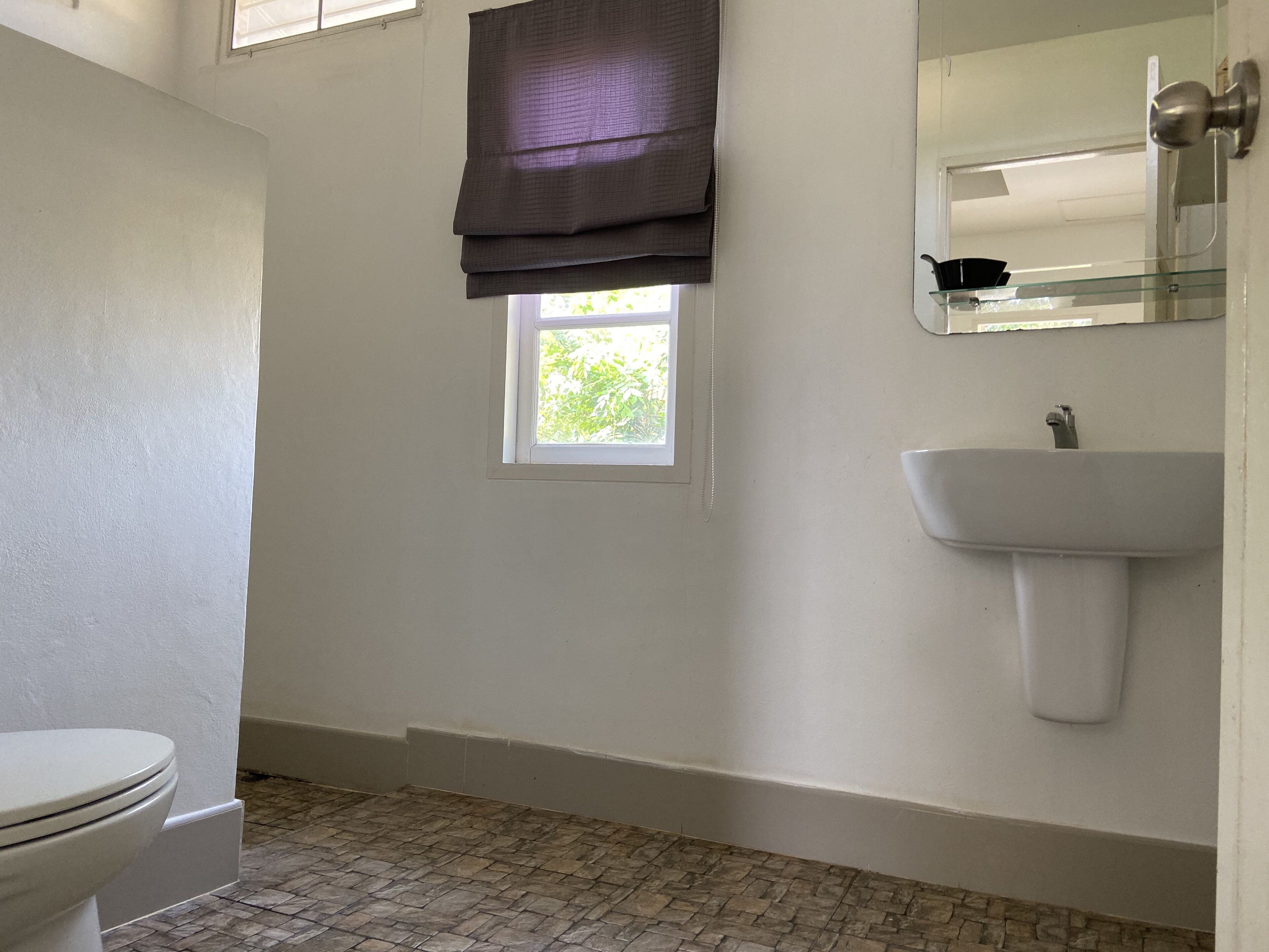 Un baño con inodoro, ventana, lavabo y espejo.