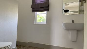 Un baño con inodoro, ventana, lavabo y espejo.