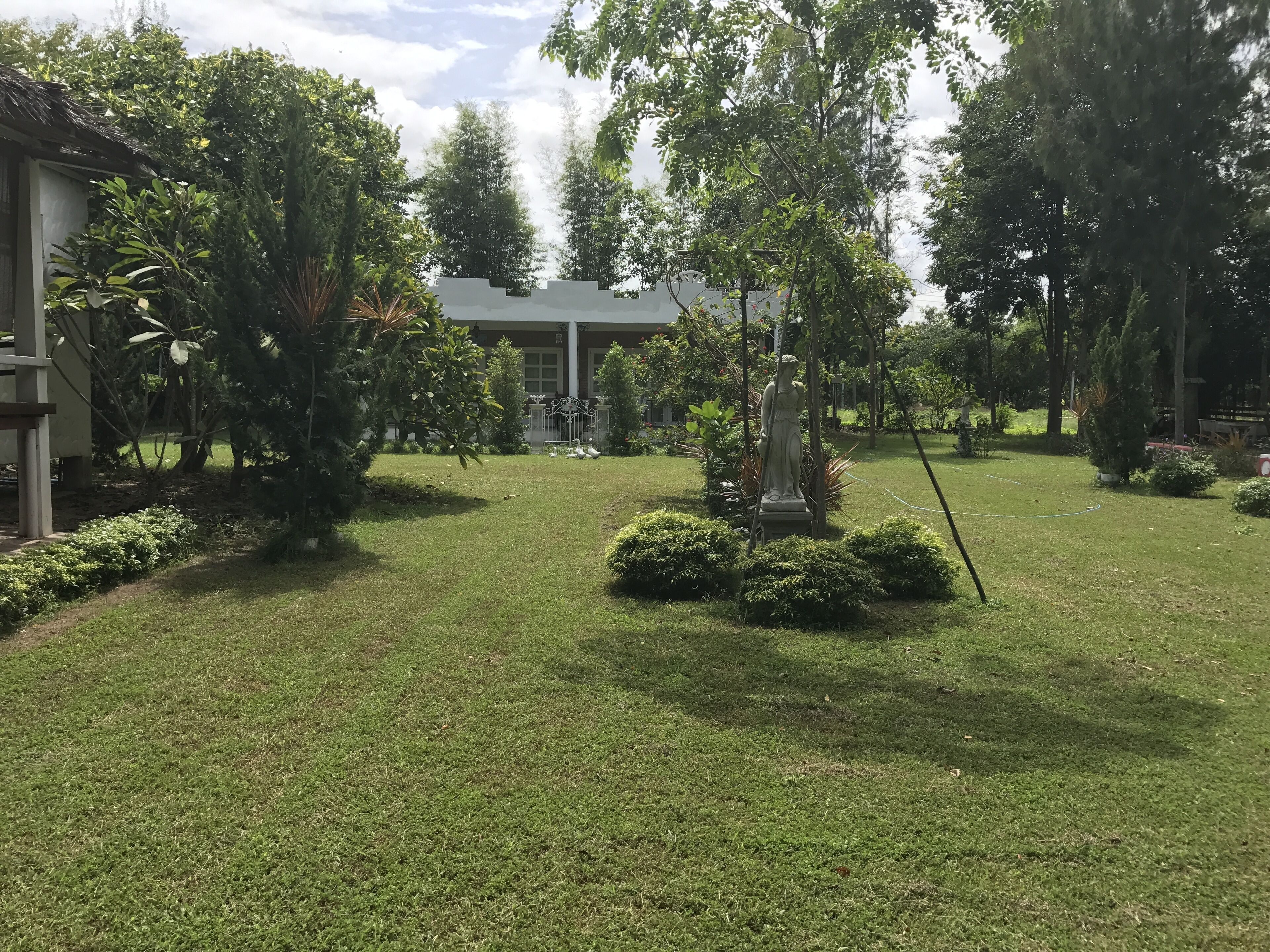 A well-maintained garden with a statue, a building in the background, and a clear sky.