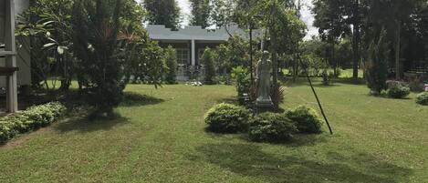 A well-maintained garden with a statue, a building in the background, and a clear sky.