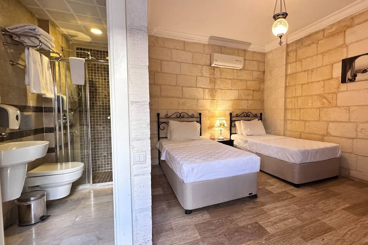 Een kamer met een badkamer, twee bedden, een houten stoel en een spiegel aan de muur.