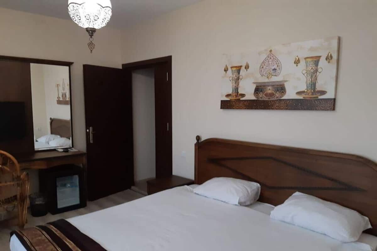 Een slaapkamer met een houten bed, een bureau met stoel, een televisie en een wanddecoratie van vazen.