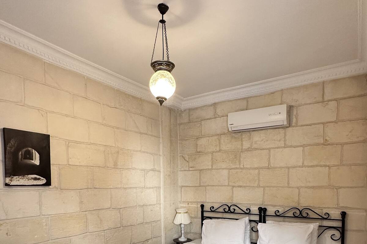 Een slaapkamer met een bed, nachtkastje, lamp en een wandairconditioner.