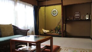 A traditional Japanese-style living room with tatami flooring, a low wooden table, a green sofa, and a sliding door with a decorative hanging.