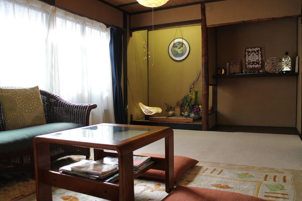 A traditional Japanese-style living room with tatami flooring, a low wooden table, a green sofa, and a sliding door with a decorative hanging.