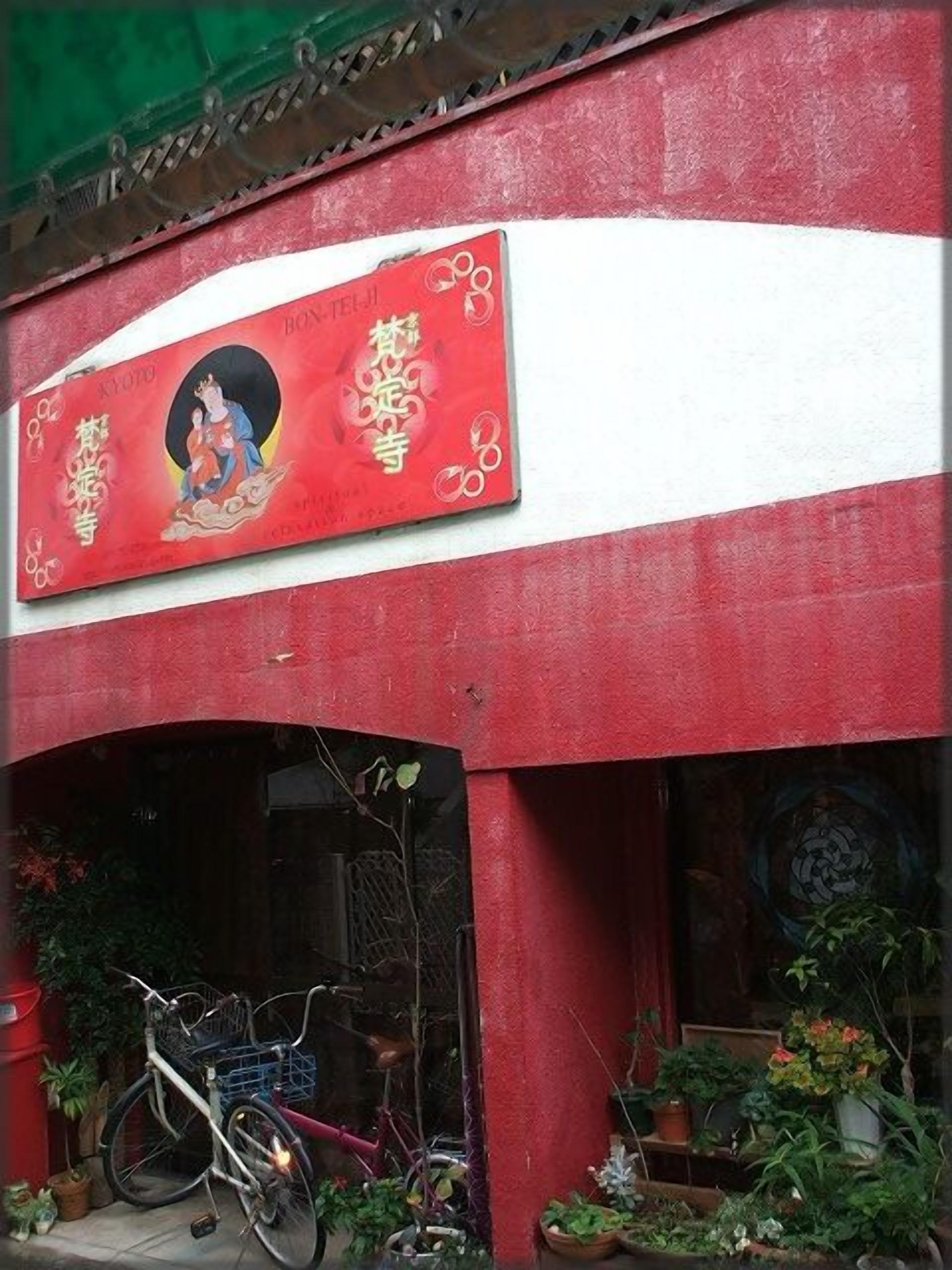 A building with a red and white facade, a bicycle parked outside, and various potted plants.