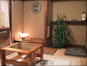 Une pièce de style japonais traditionnel, avec un sol recouvert de tatamis, une petite table en bois sur laquelle se trouve une lampe, une plante en pot et une étagère ornée d’objets décoratifs.