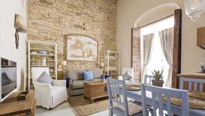 A cozy living room with a brick wall, a white sofa, a wooden coffee table, and a dining area with blue chairs and a table. - Hotel Casa de las Cuatro Torres (Cádiz)