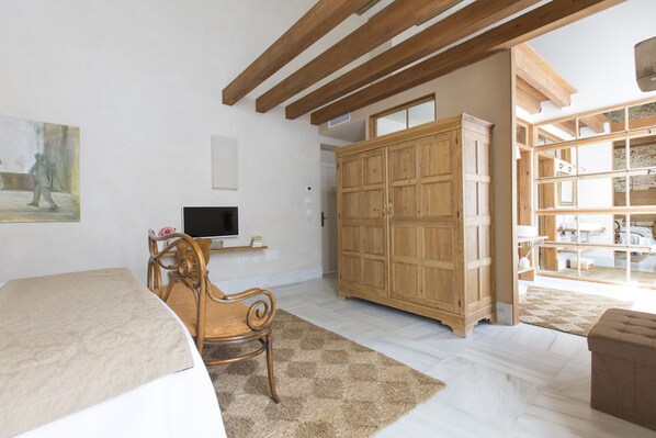 Un dormitorio con cama, una silla de madera, televisión, armario y un ventanal grande.