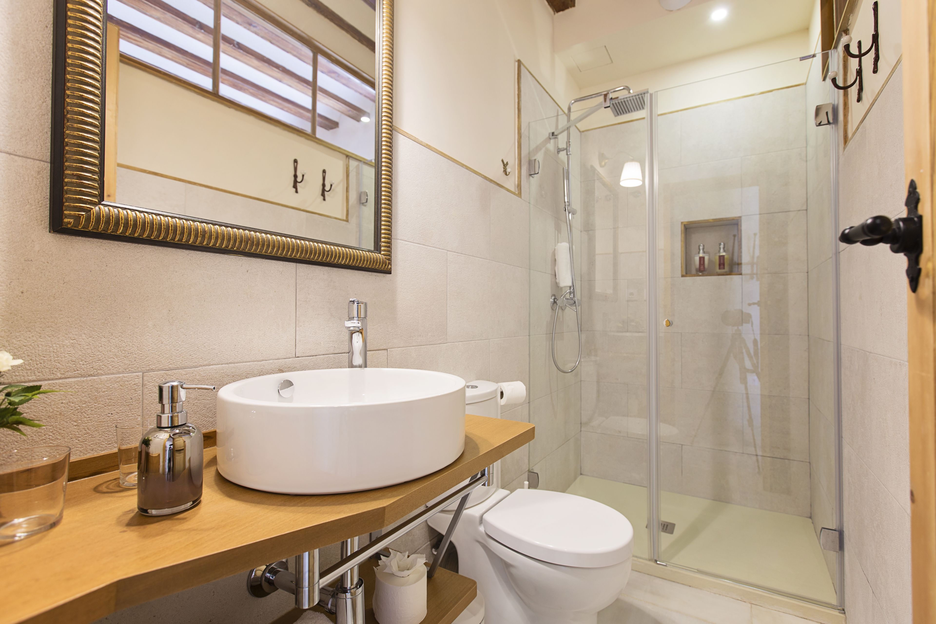 A bathroom with a large mirror, a round sink, a toilet, and a glass-enclosed shower.