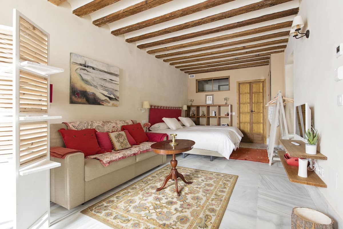 A room with a bed, a sofa, a small table, and a painting on the wall.