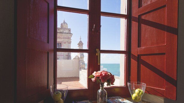 A window with a view of a building and the sea. - Hotel Casa de las Cuatro Torres (Cádiz)