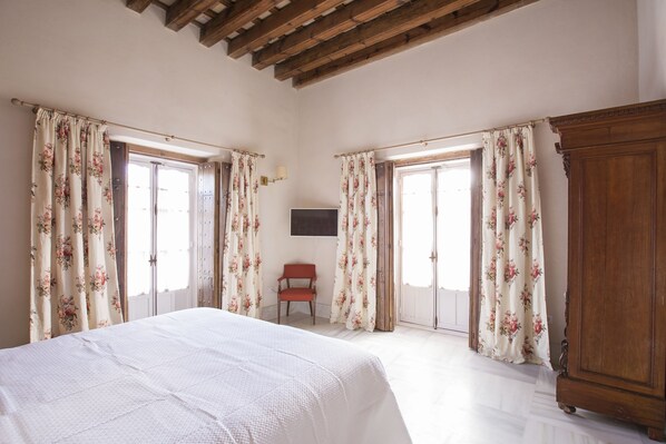 A bedroom with a wooden ceiling, a bed, a chair, and a wardrobe. - Hotel Casa de las Cuatro Torres (Cádiz)