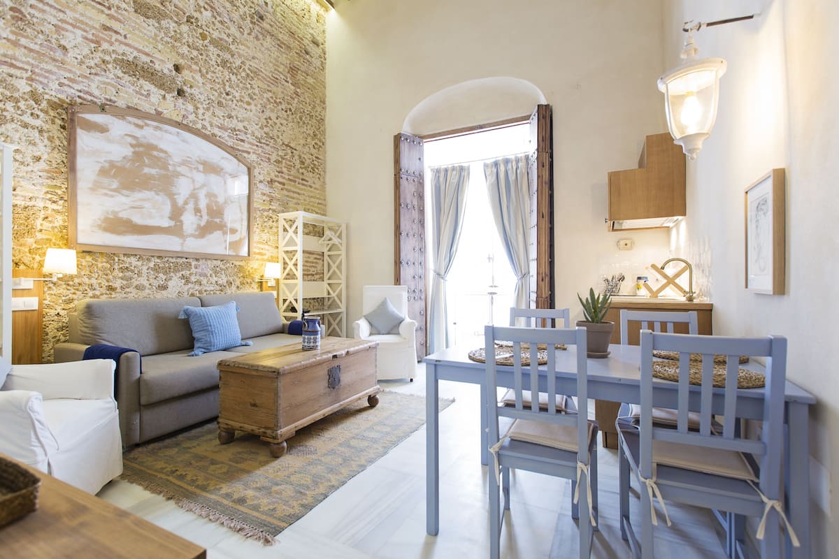 A cozy living room with a stone wall, a wooden coffee table, a sofa, and a dining area with chairs and a table.