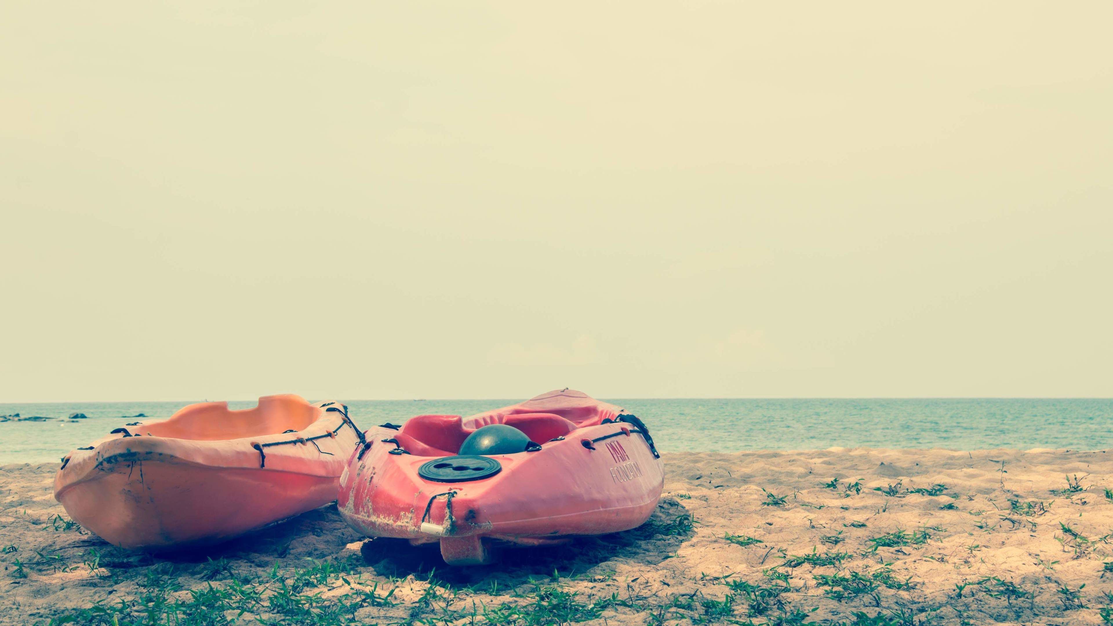 Dos kayaks rosados en una playa arenosa, con el océano al fondo.