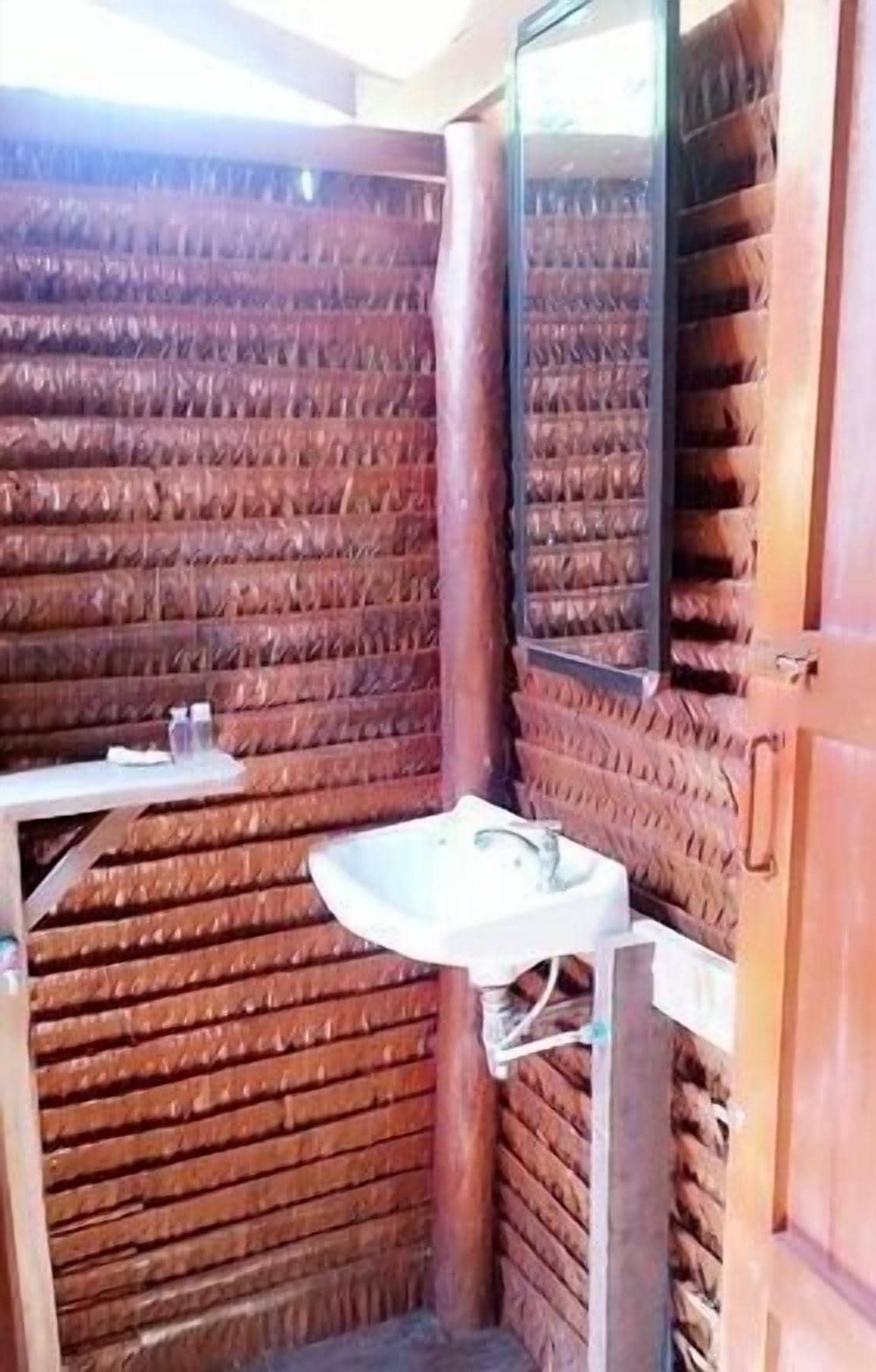 A small, rustic bathroom with a wooden slatted wall, a single sink, and a mirror.