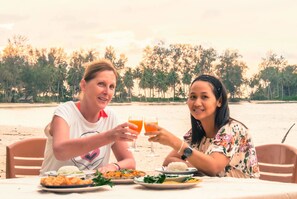 Two people sitting at a table with food and drinks, overlooking a beach with palm trees. - Rakkan Resort (Khura Buri)