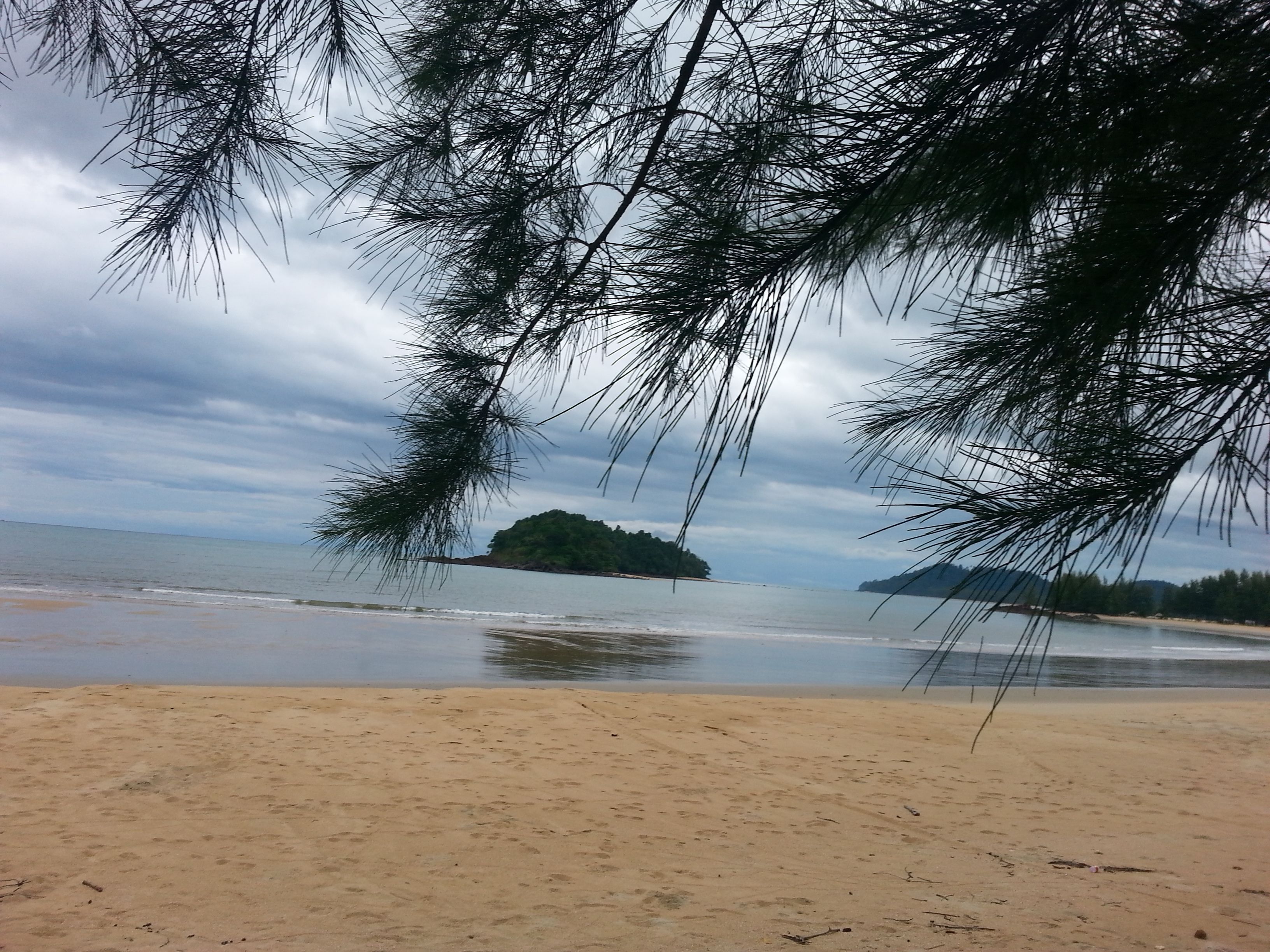 A beach with a sandy shore, calm water, and a small island in the distance.