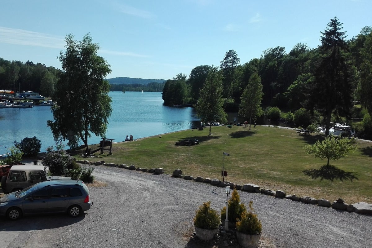 A lakeside view with boats, a grassy area, and a parking lot.