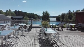 A wooden deck with tables and chairs overlooking a lake. - Alcatraz (Gustavsfors)