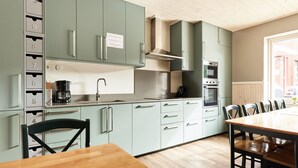 A modern kitchen with light green cabinets, a wooden dining table, and a built-in oven. - Alcatraz (Gustavsfors)