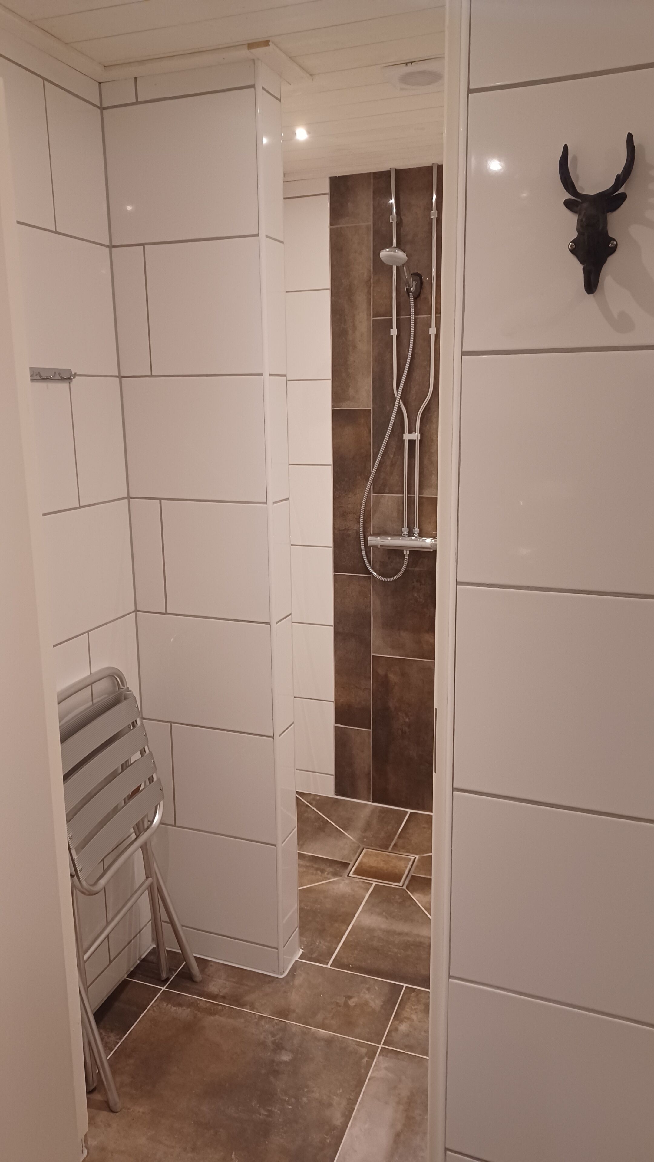 A bathroom with white tiled walls, a shower with a handheld showerhead, and a towel rack.