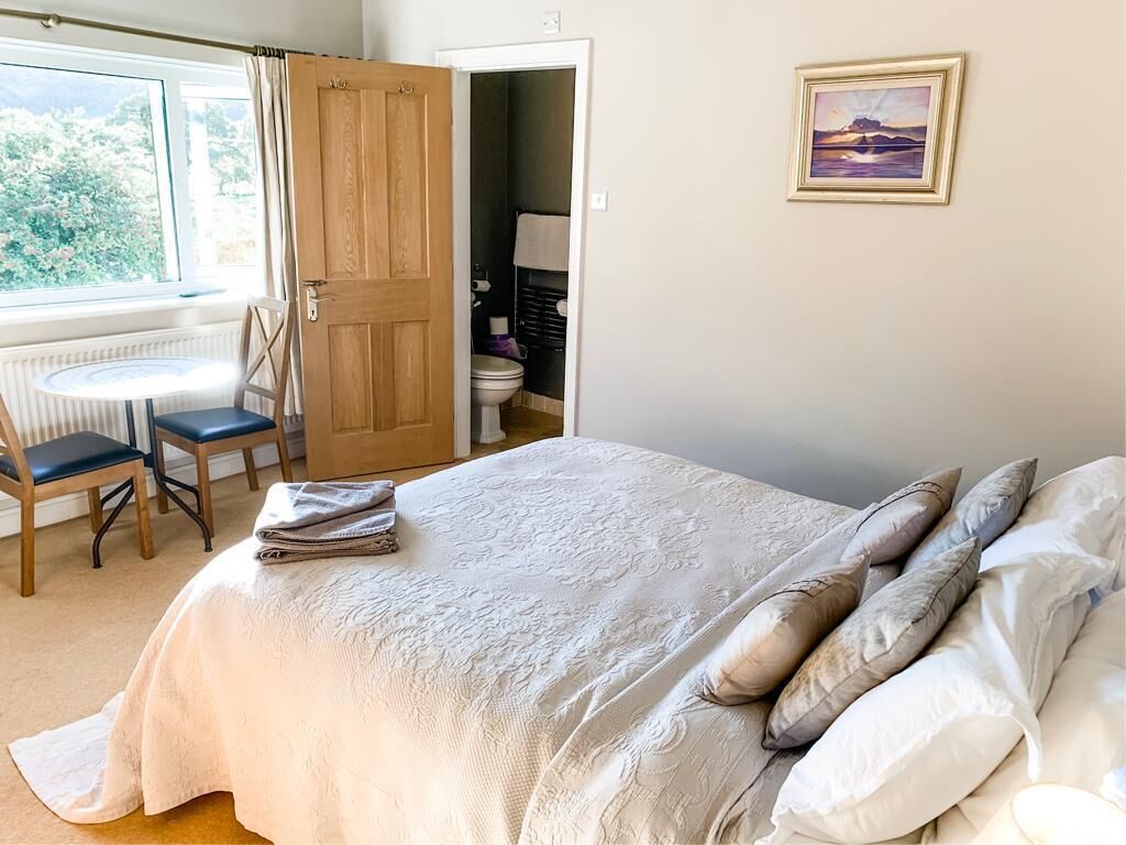 Un dormitorio con cama, almohadas, una silla, una mesa y vistas al exterior.