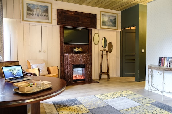 A cozy living room with a fireplace, a laptop on a table, and a bookshelf. - Domaine du Lieu des Brocs (Brucourt)