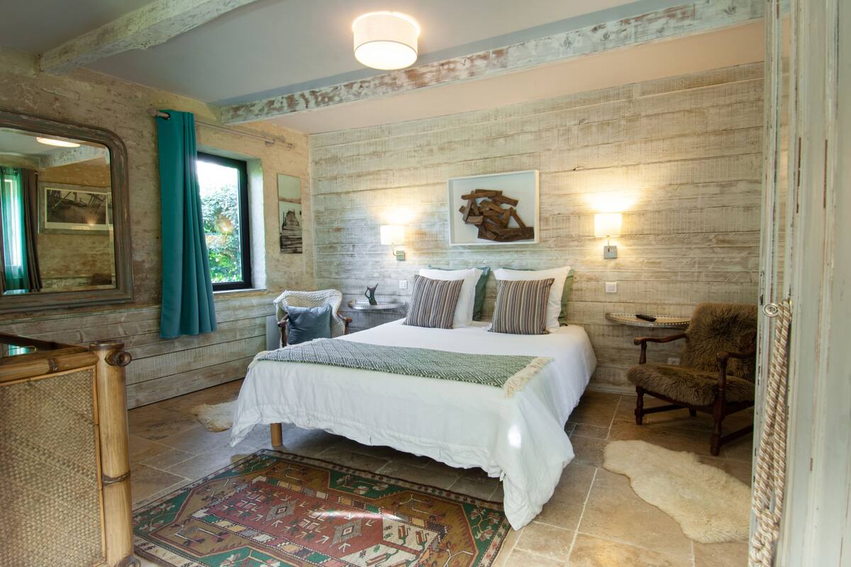 Een slaapkamer met een groot bed, een stoel, een vloerkleed en een houten wand.