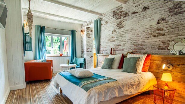 Een slaapkamer met een bed, een stoel, een klein tafeltje en een lamp.