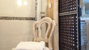Een badkamer met een witte badkuip, een douche, een witte stoel met een handdoek, en een houten scheidingswand.