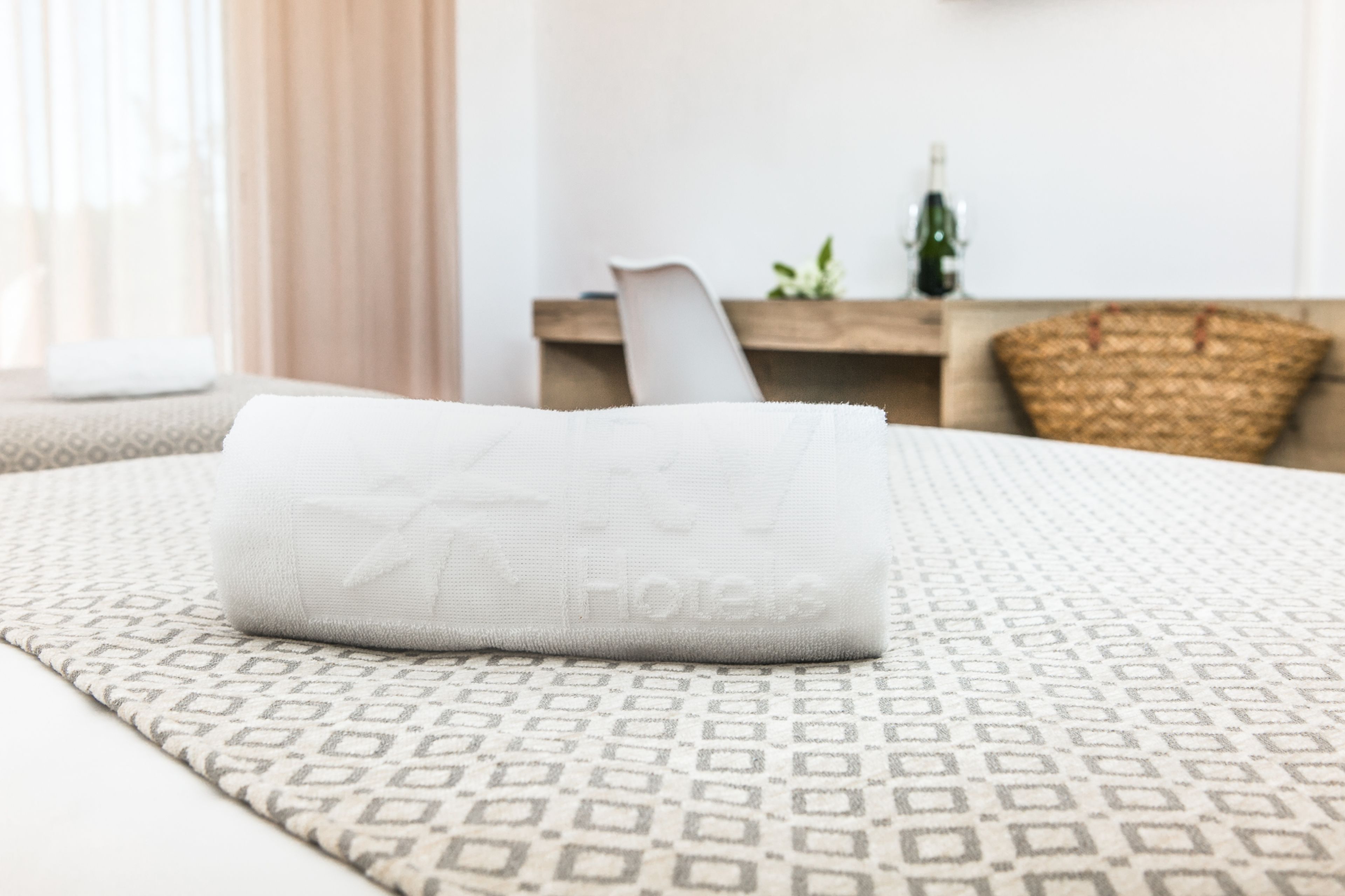 Toalha branca dobrada em uma cama com colcha estampada em quarto de hotel.