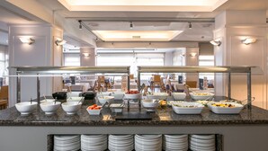 A buffet setup with various food bowls and plates, a counter with a glass display case, and a seating area in the background.