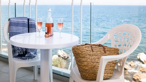 A balcony with a white table, two chairs, a bottle of wine, and glasses.