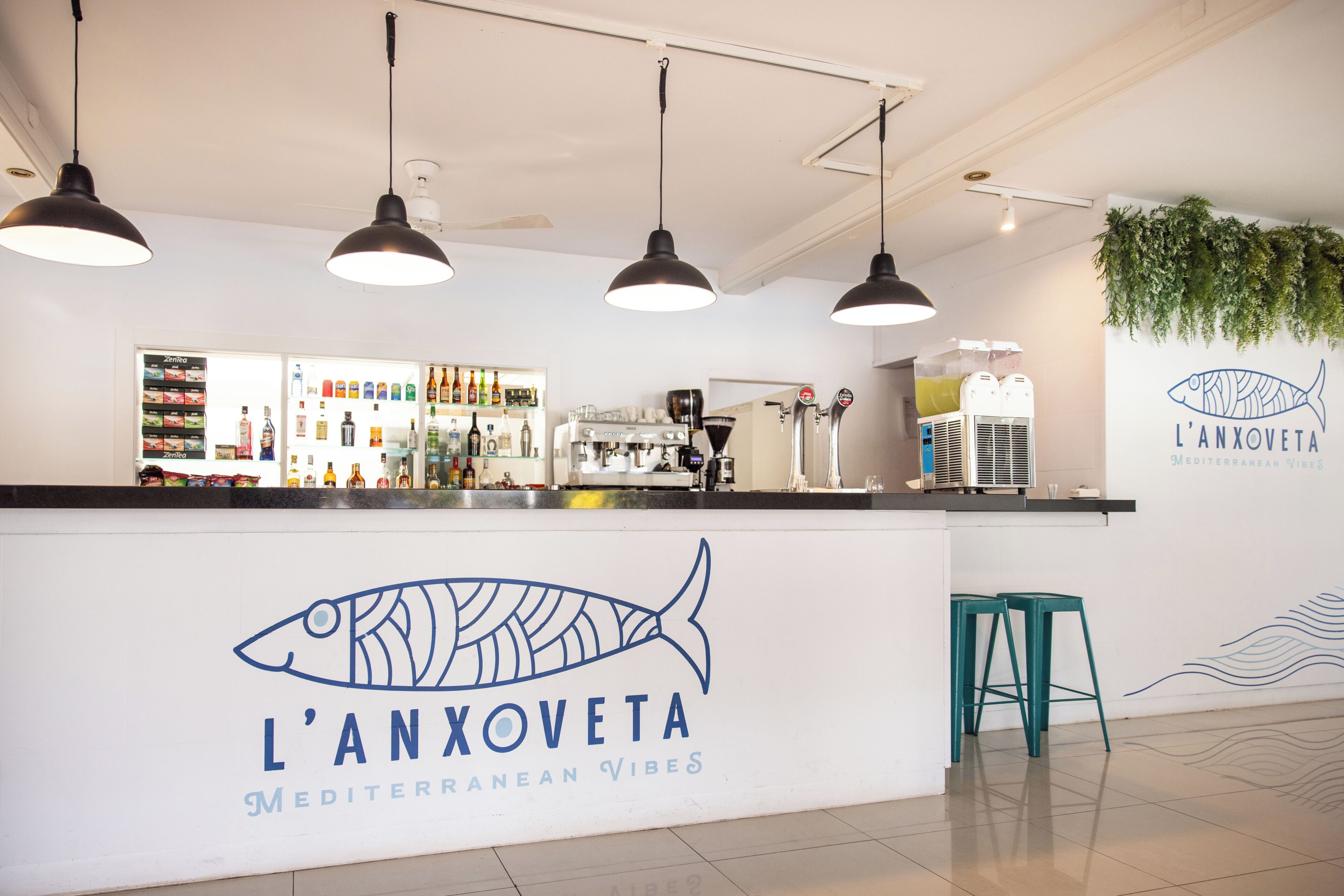 Zona de bar con barra, luces colgantes y una pared con el logotipo de un pez y texto.
